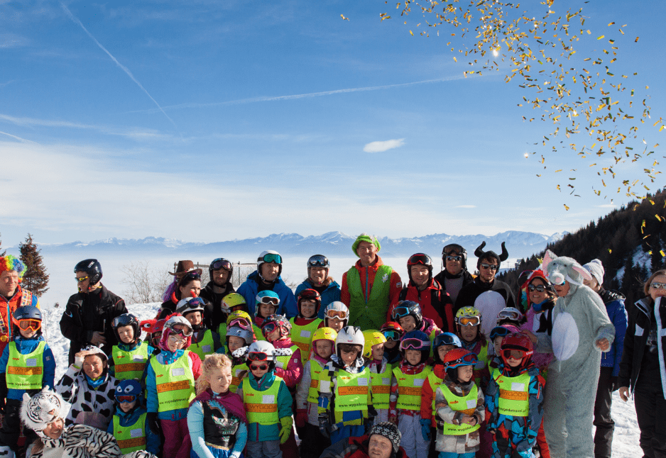 Zdjęcie grupowe małych narciarzy na szczycie góry.