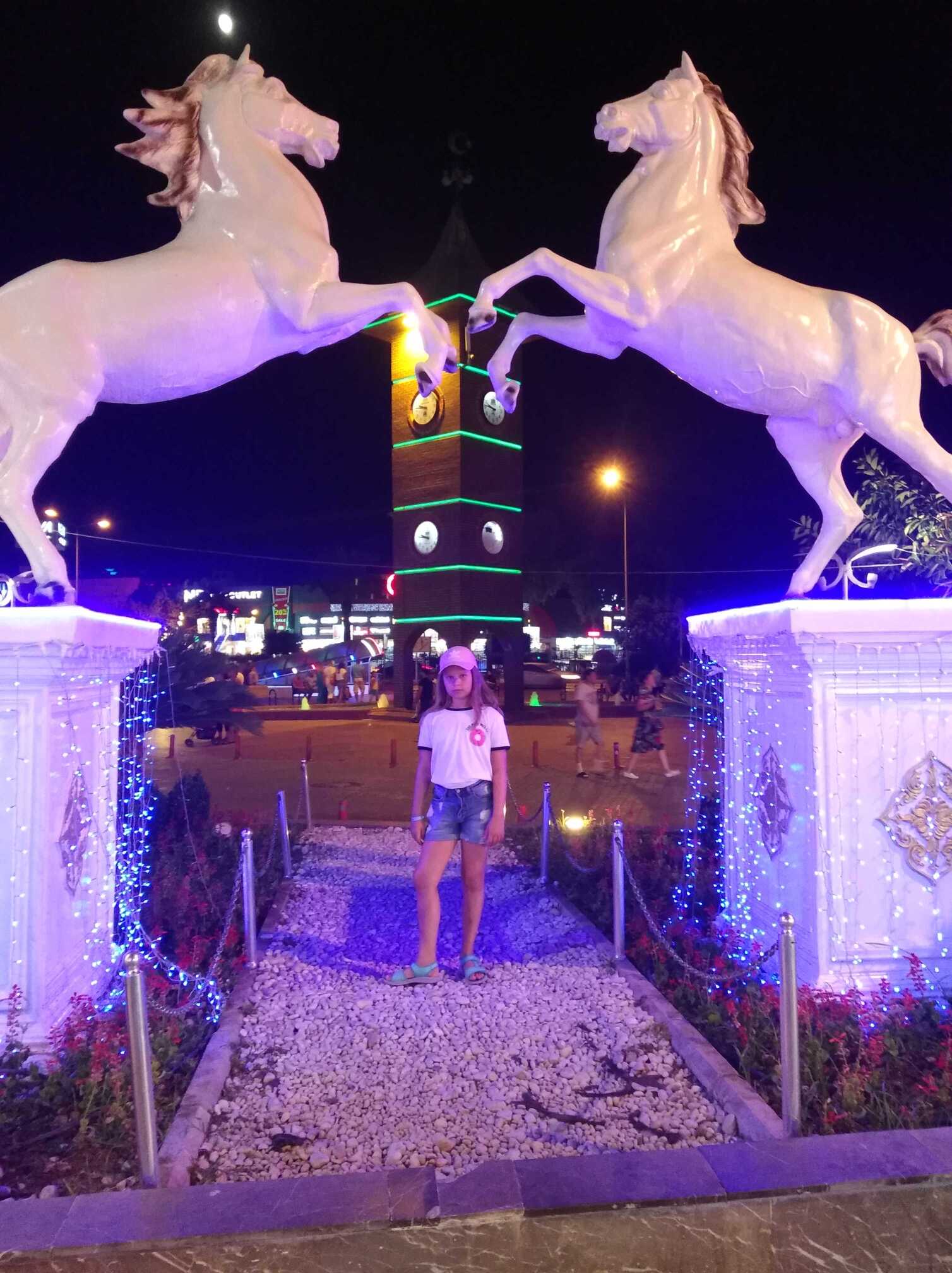 Młoda dziewczynaka na tle wierzy zegarowej nocą.